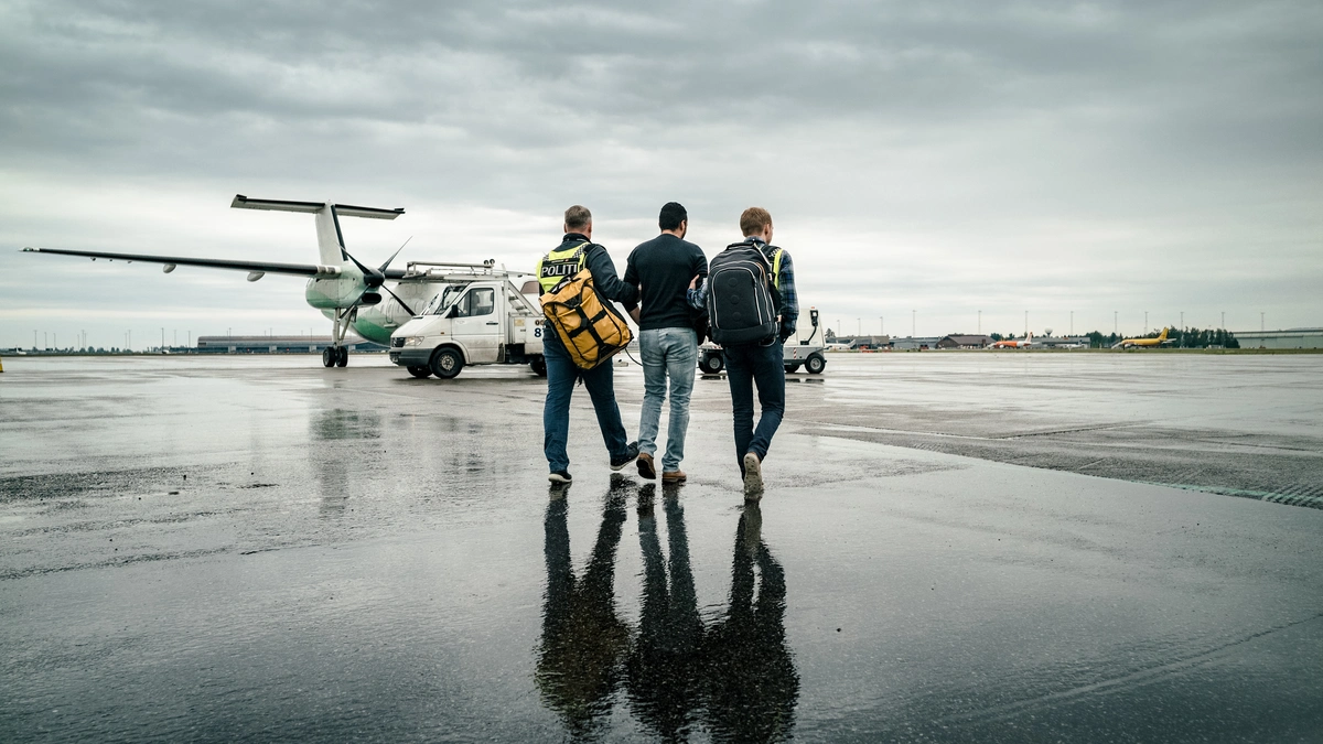 To personer fra politiet følger en person til et fly. Foto.
